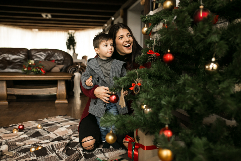 A mother and her young child smiling joyfully as they decorate a Christmas tree inside their home in Indio, CA, surrounded by holiday ornaments.